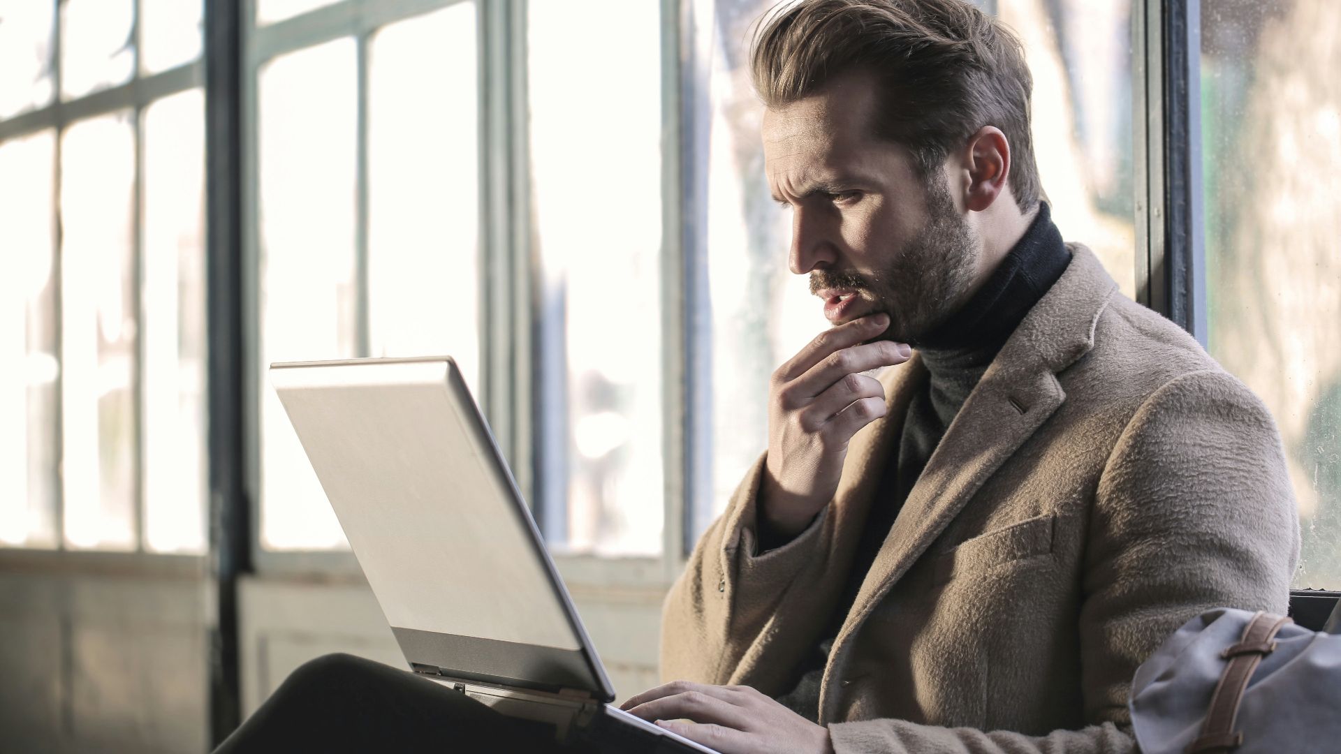 man holding his chin facing laptop computer