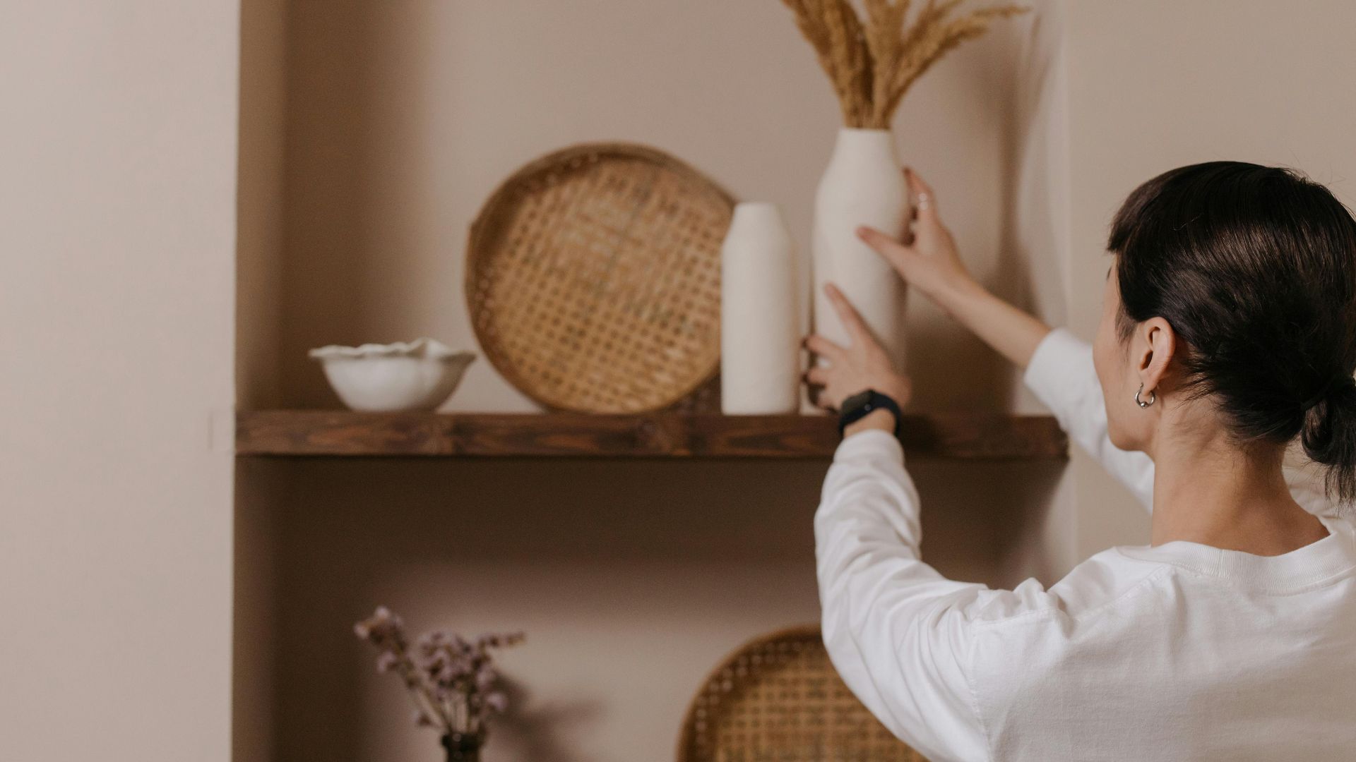 A woman arranging vases on a rustic shelf, highlighting minimalist interior design.