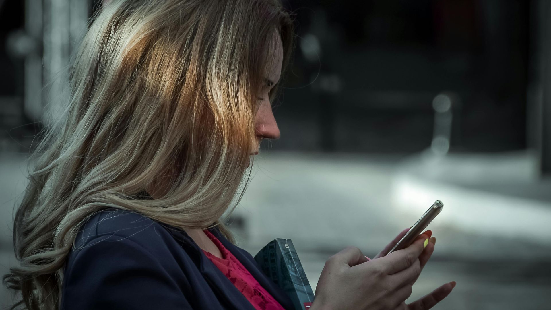 Side profile of a young woman texting on her smartphone in a shaded outdoor area.