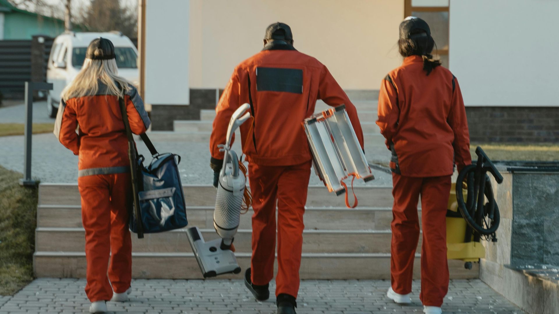 Cleaning crew in red uniforms with equipment approaching a modern house exterior.