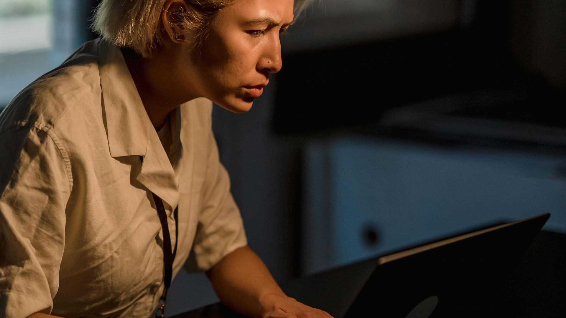 A businesswoman deeply engaged in work while typing on a laptop in a dimly lit office environment.