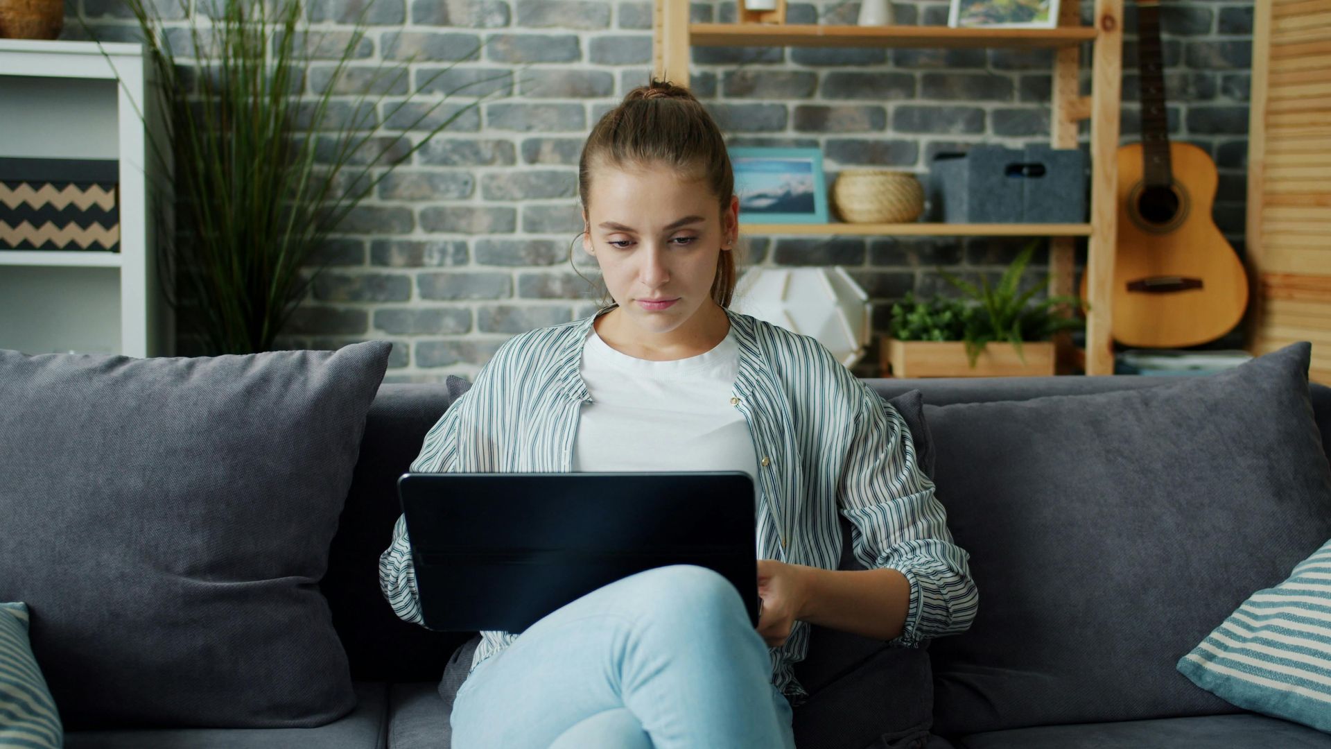 Young woman sitting on a sofa using a laptop in a home setting.