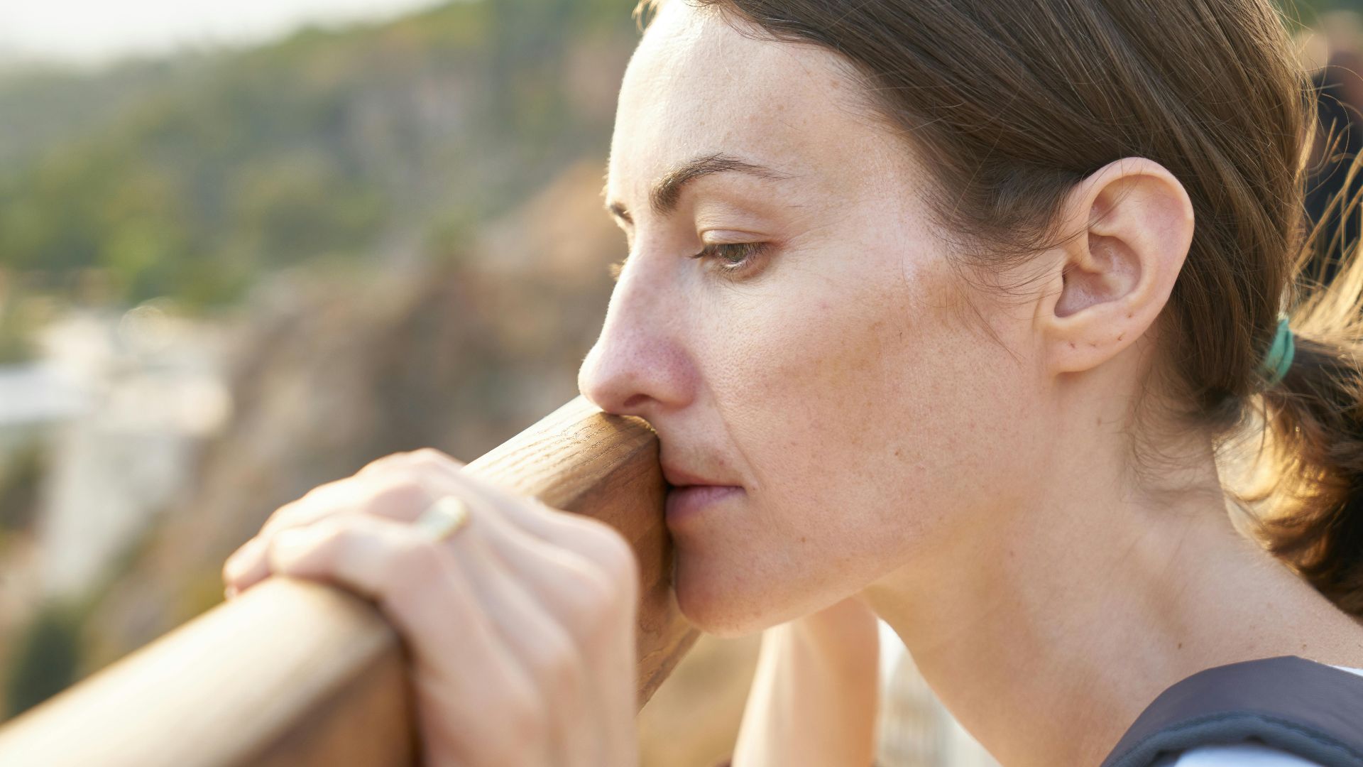 A thoughtful woman leans on a railing, lost in deep contemplation outdoors.