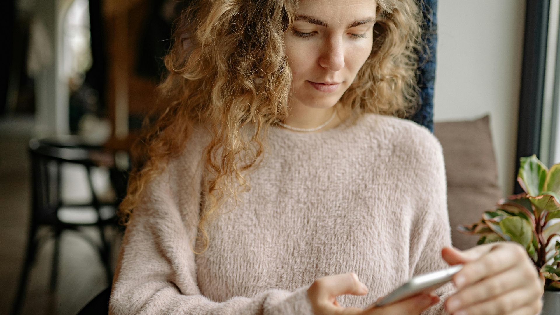 A woman in a cozy sweater using a smartphone in a relaxed indoor environment.