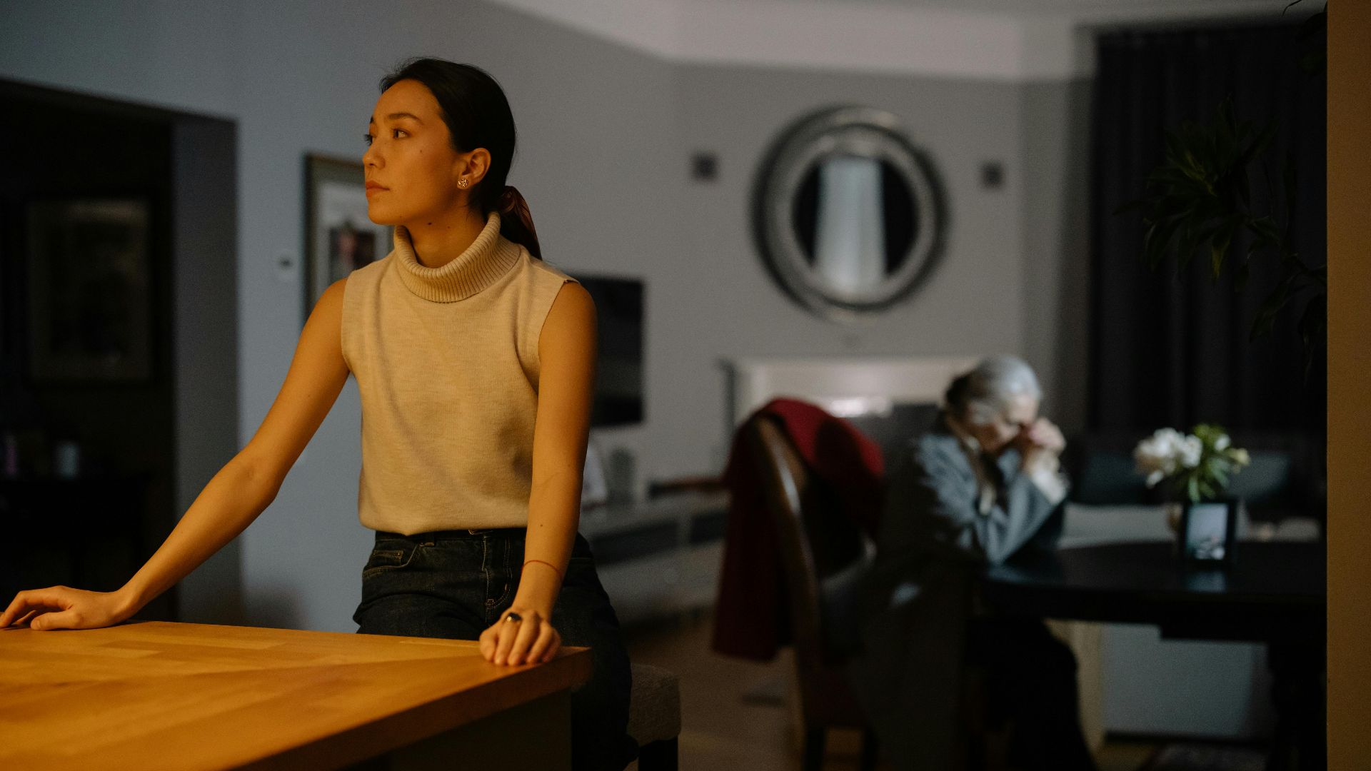 Tense moment between two women in a dimly lit living room, capturing emotion and introspection.