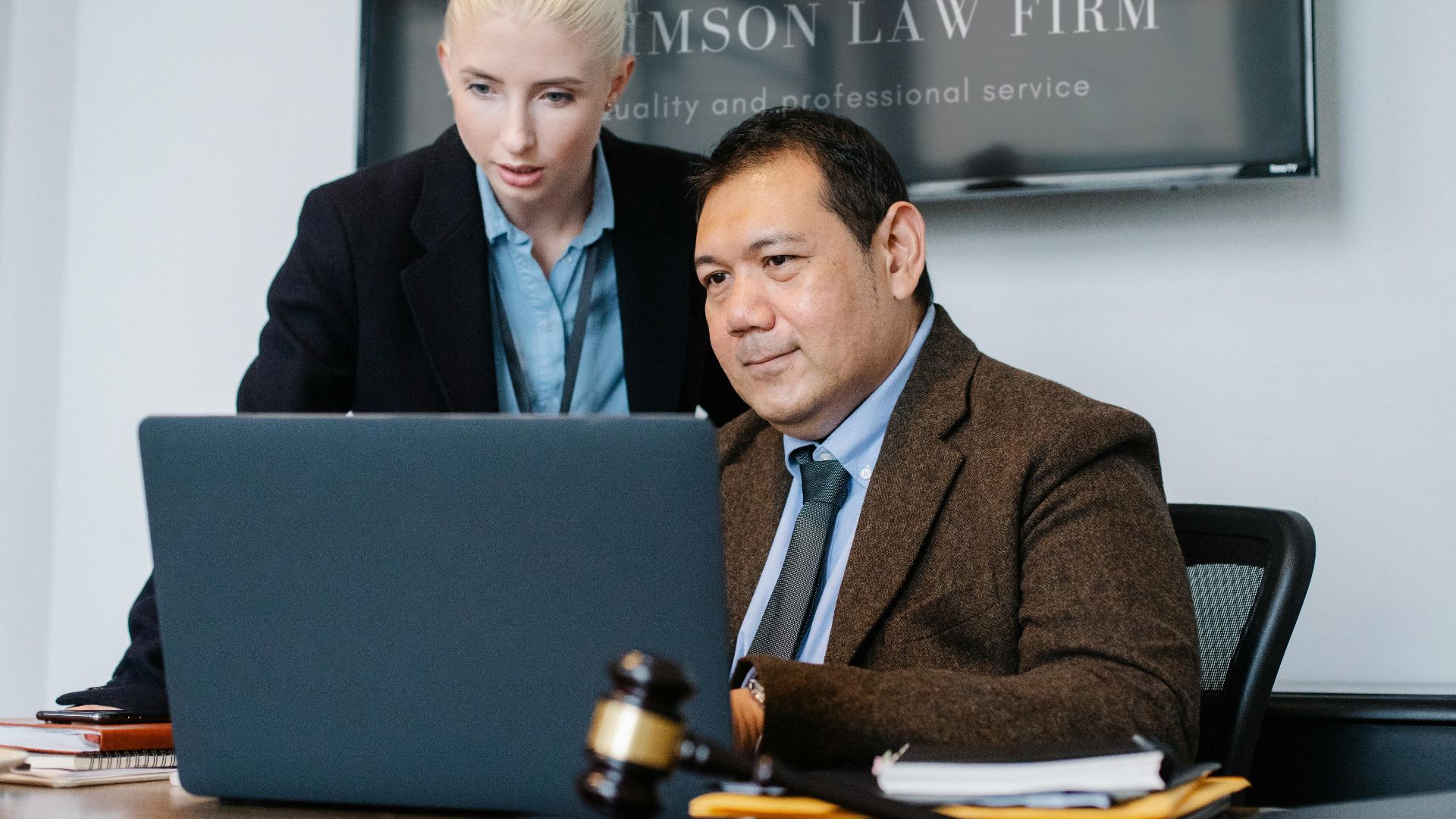 Smart mature ethnic judge in suit working on laptop and discussing details of new case with young female assistant in law firm