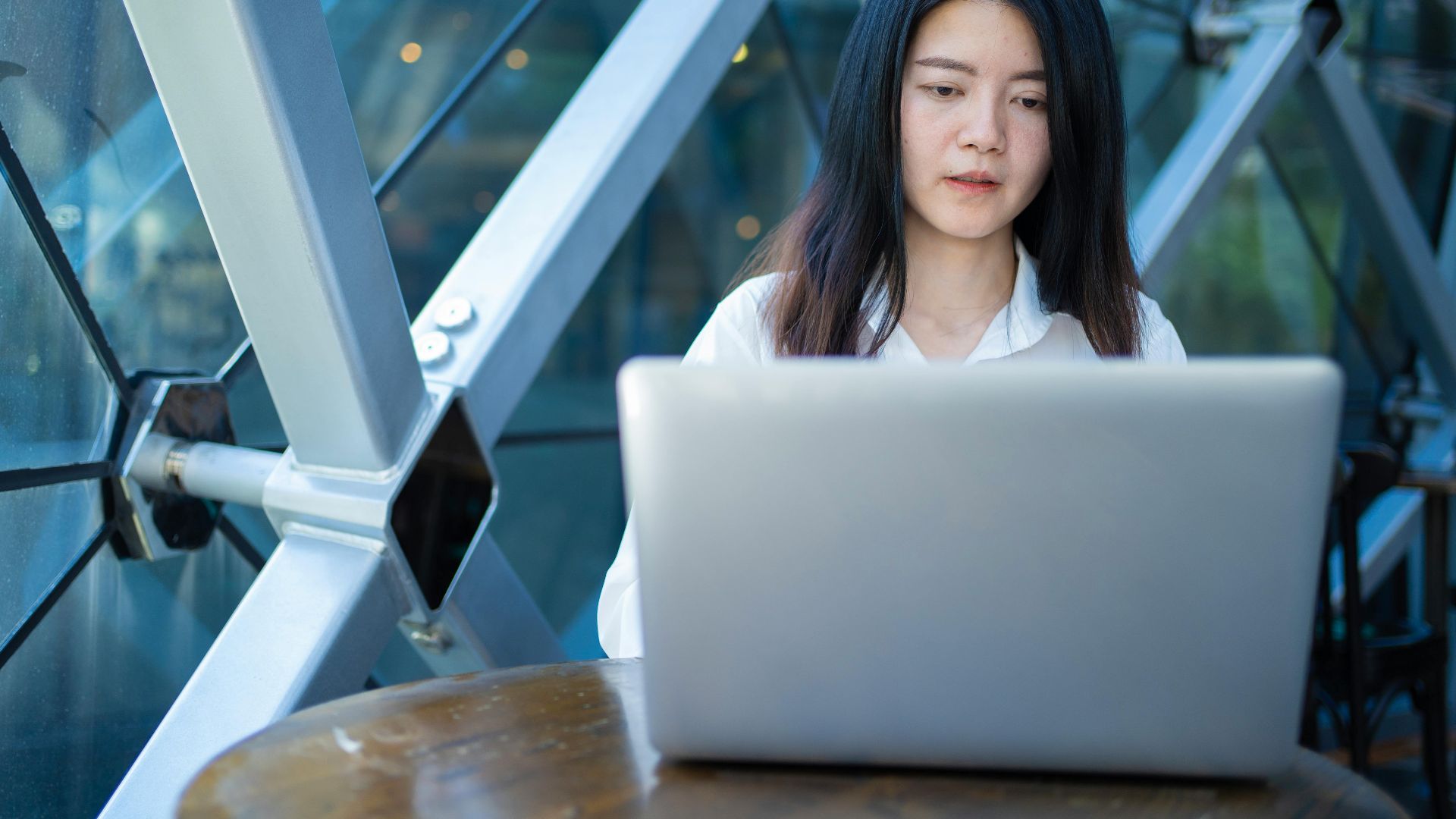 Confident Asian woman working on laptop in a modern indoor space, focused on remote business tasks.