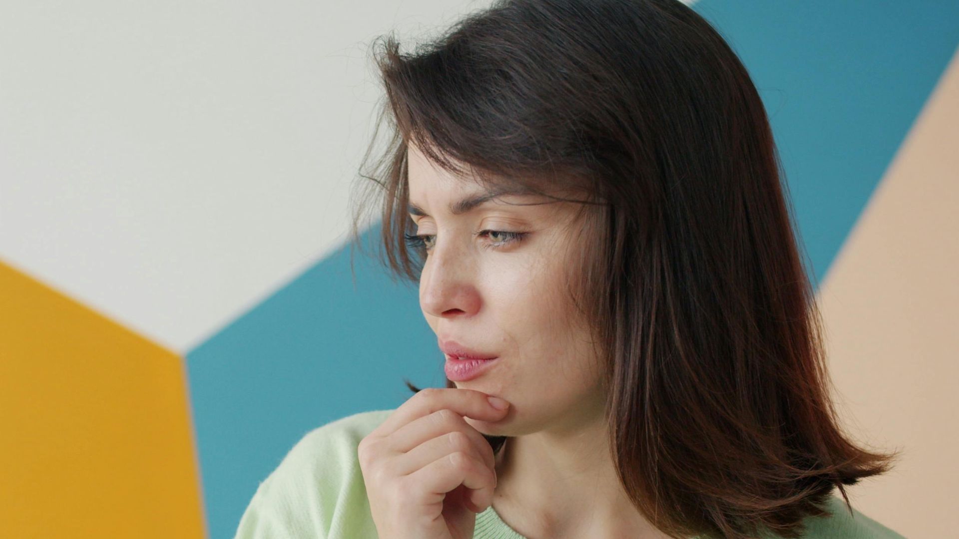 Young woman in contemplation against a colorful geometric background, indoors.