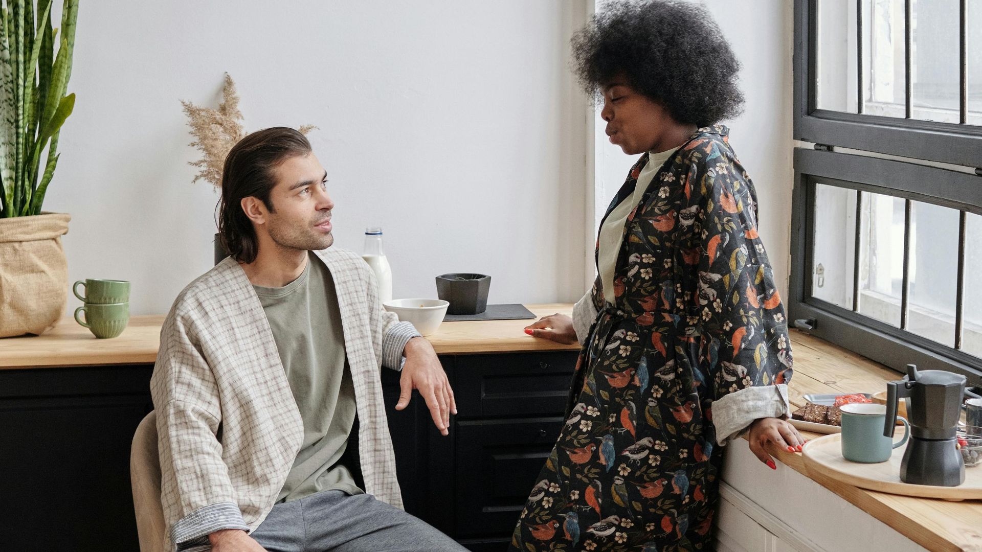 An interracial couple enjoying a relaxed morning conversation by the window in their cozy home.