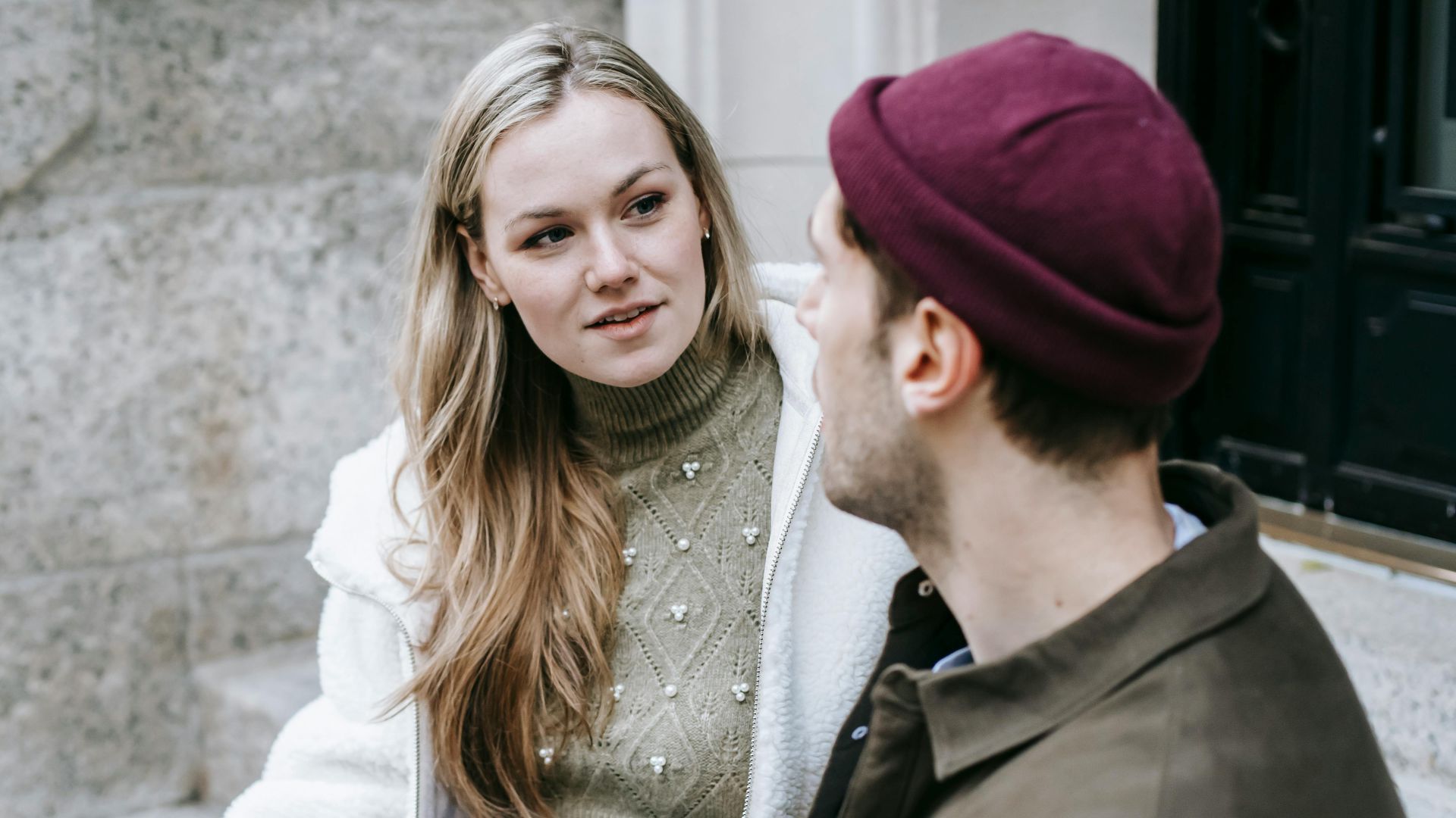 Man and woman talking sitting on steps outside house and having hot beverage in paper cups
