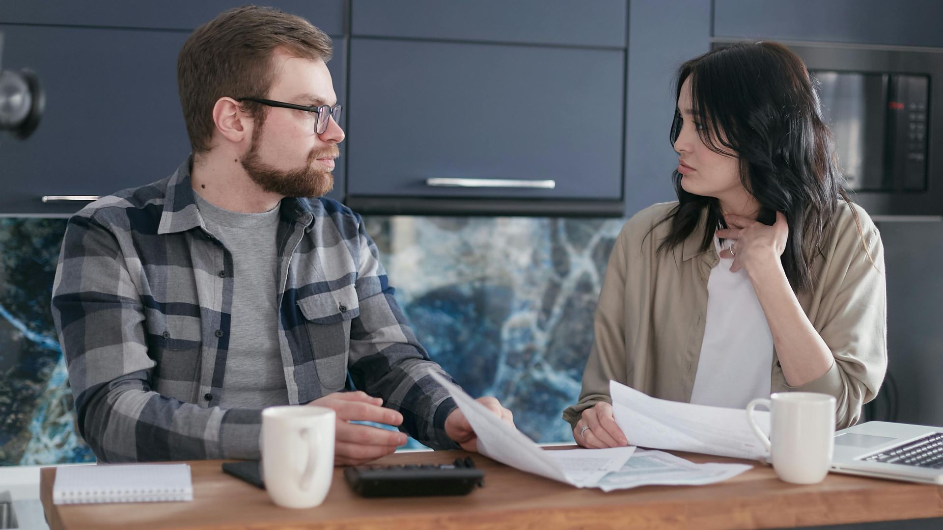 A young couple sitting at a table discussing bills and financial plans in a modern kitchen.