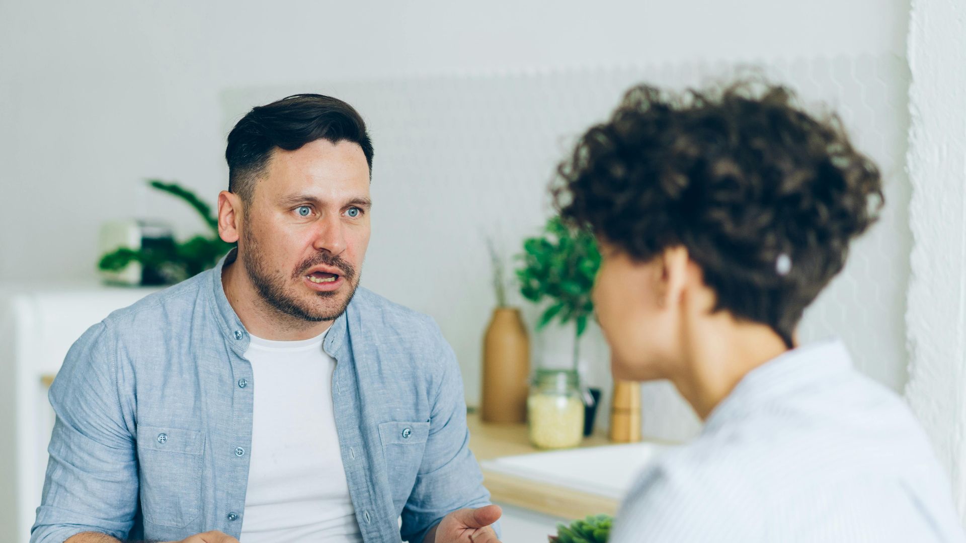 Couple having a serious conversation at the kitchen table with coffee cups.
