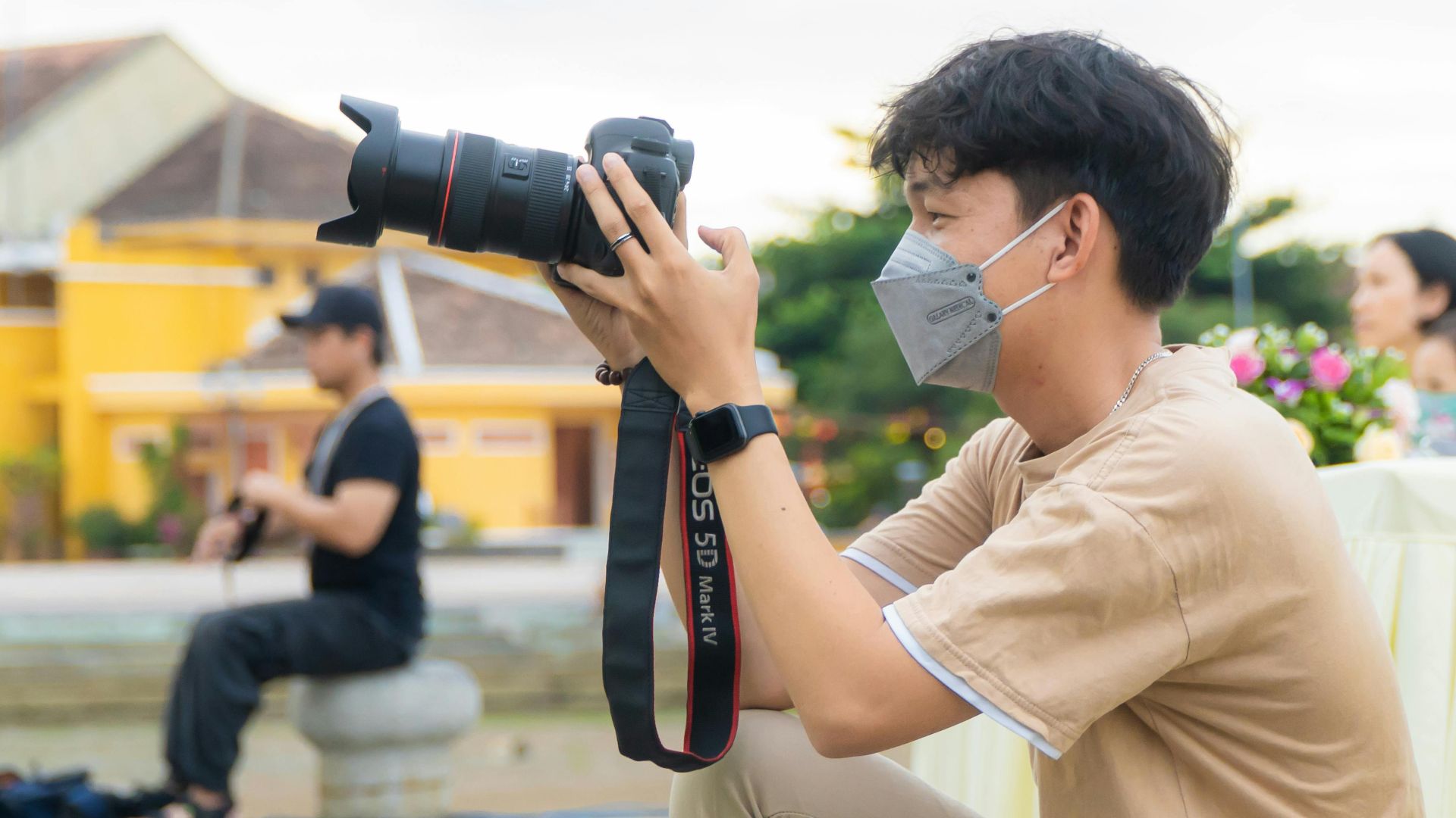 A photographer wearing a mask takes photos at an outdoor event, capturing candid moments.