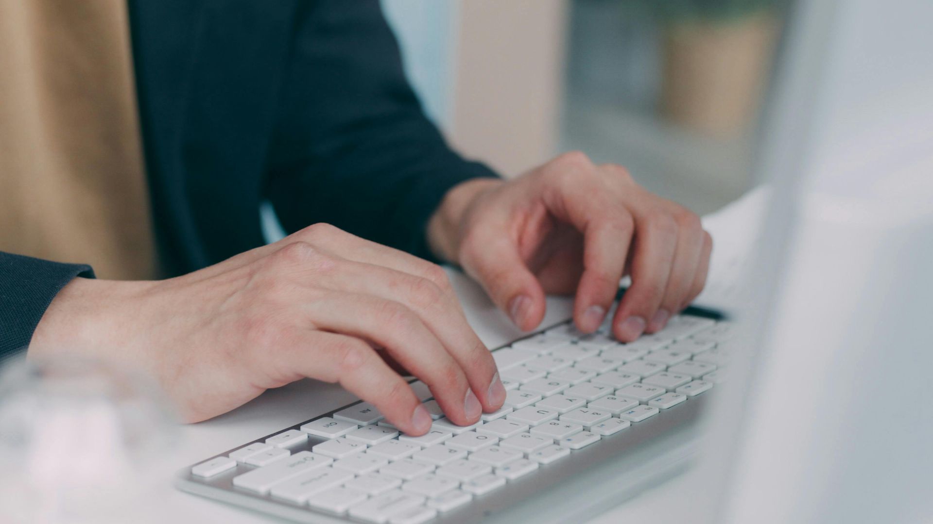 Close-up of hands typing on a white keyboard in an office setting. Ideal for business or technology themes.