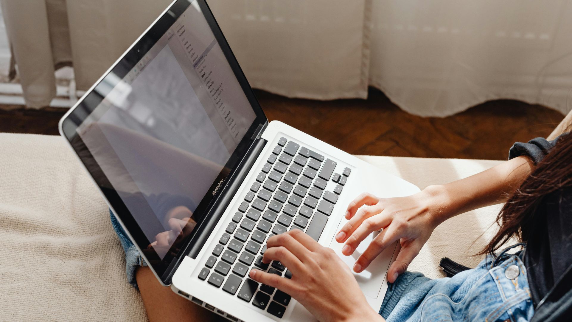 Close-up of a woman's hands typing on a laptop while sitting comfortably indoors.