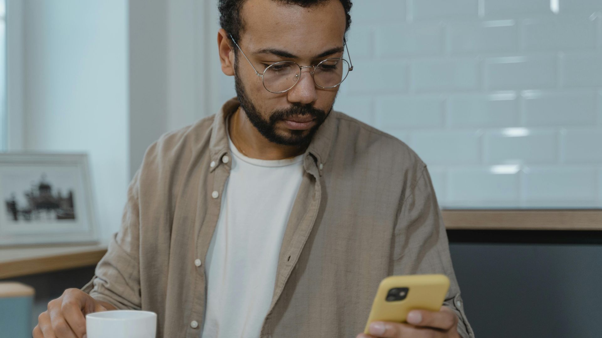 A man with eyeglasses using a smartphone while enjoying breakfast indoors. Perfect for lifestyle and technology themes.