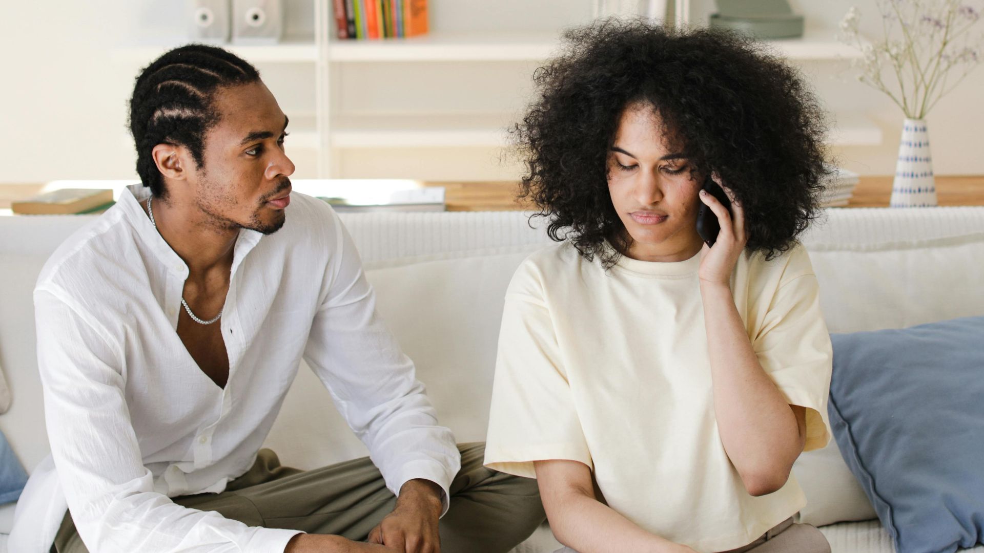 African American couple relaxing at home, sitting on sofa, talking and using phone.