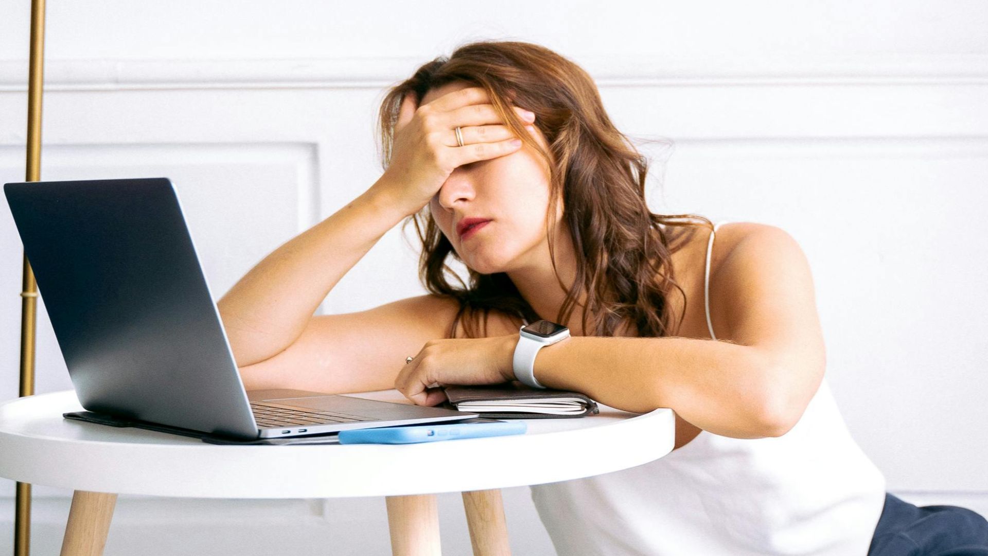 A woman showing signs of fatigue while working remotely at a laptop indoors.