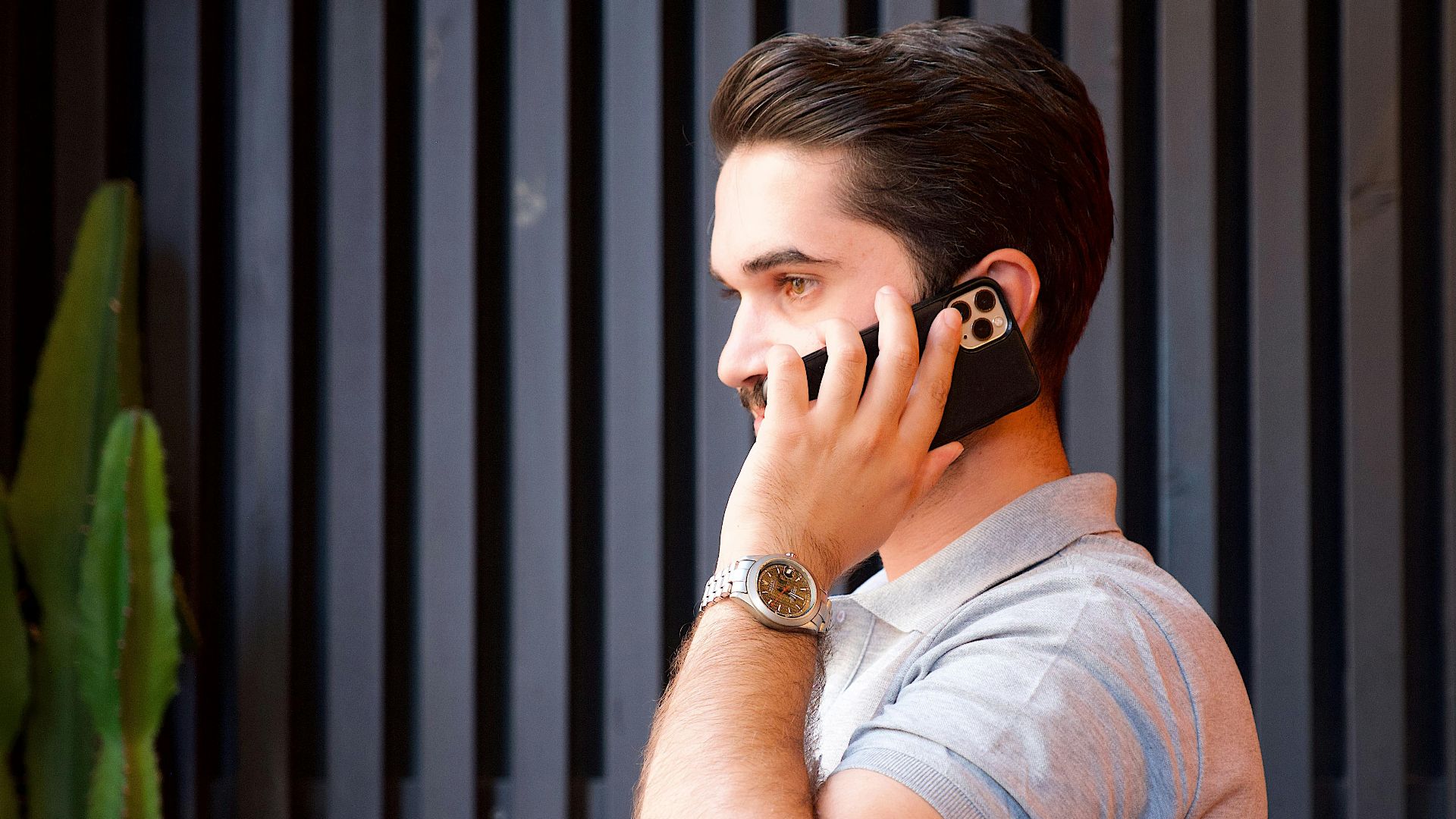 A young man in a casual shirt communicates on a smartphone while wearing a wristwatch.