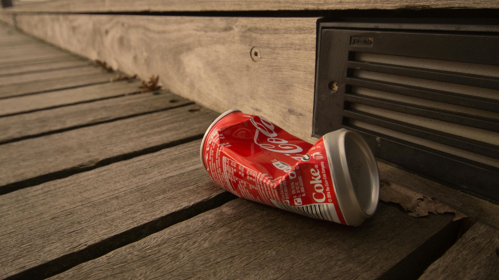 A crumpled soda can lies on a weathered wooden boardwalk, capturing urban waste.