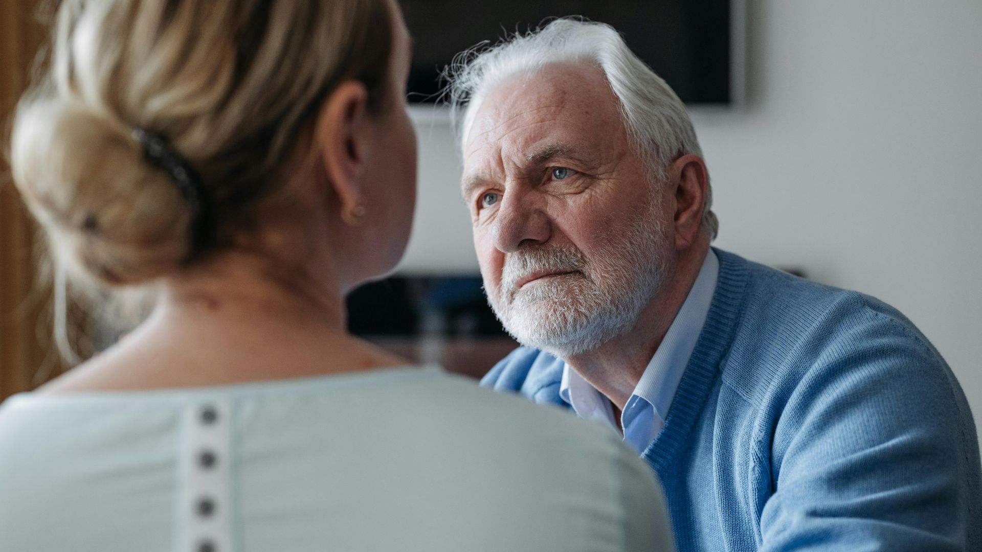 A thoughtful elderly man with grey hair having a conversation indoors, focused on a woman.