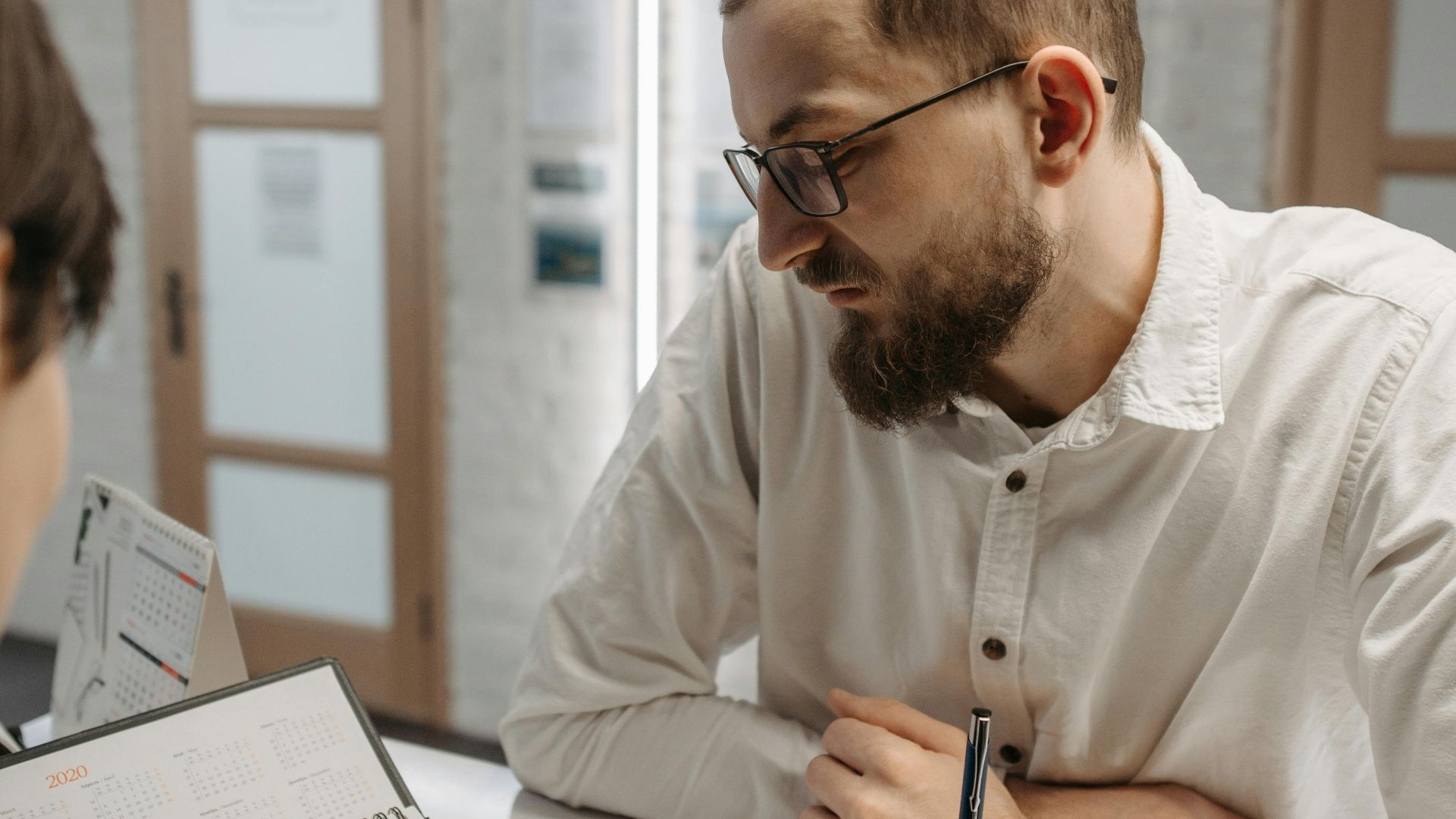 A thoughtful man leaning on a reception counter while discussing plans indoors.