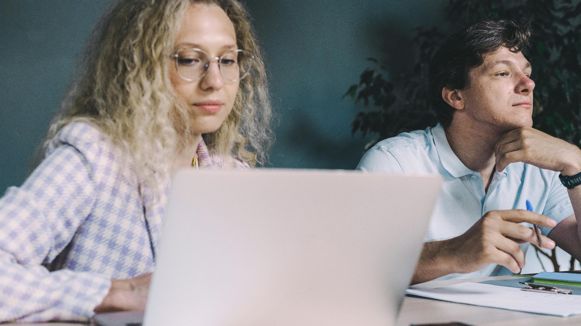 Two colleagues collaborate at a desk with laptops and papers, suggesting teamwork and productivity.