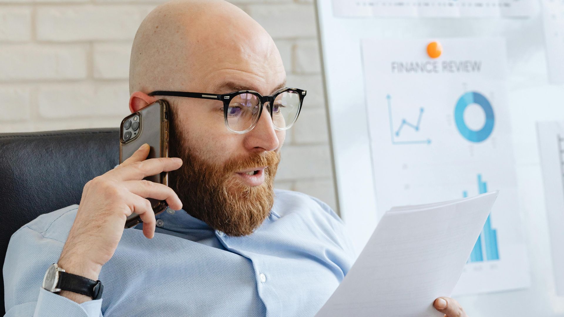 Professional analyzing data charts and graphs on paper and phone in office setting.