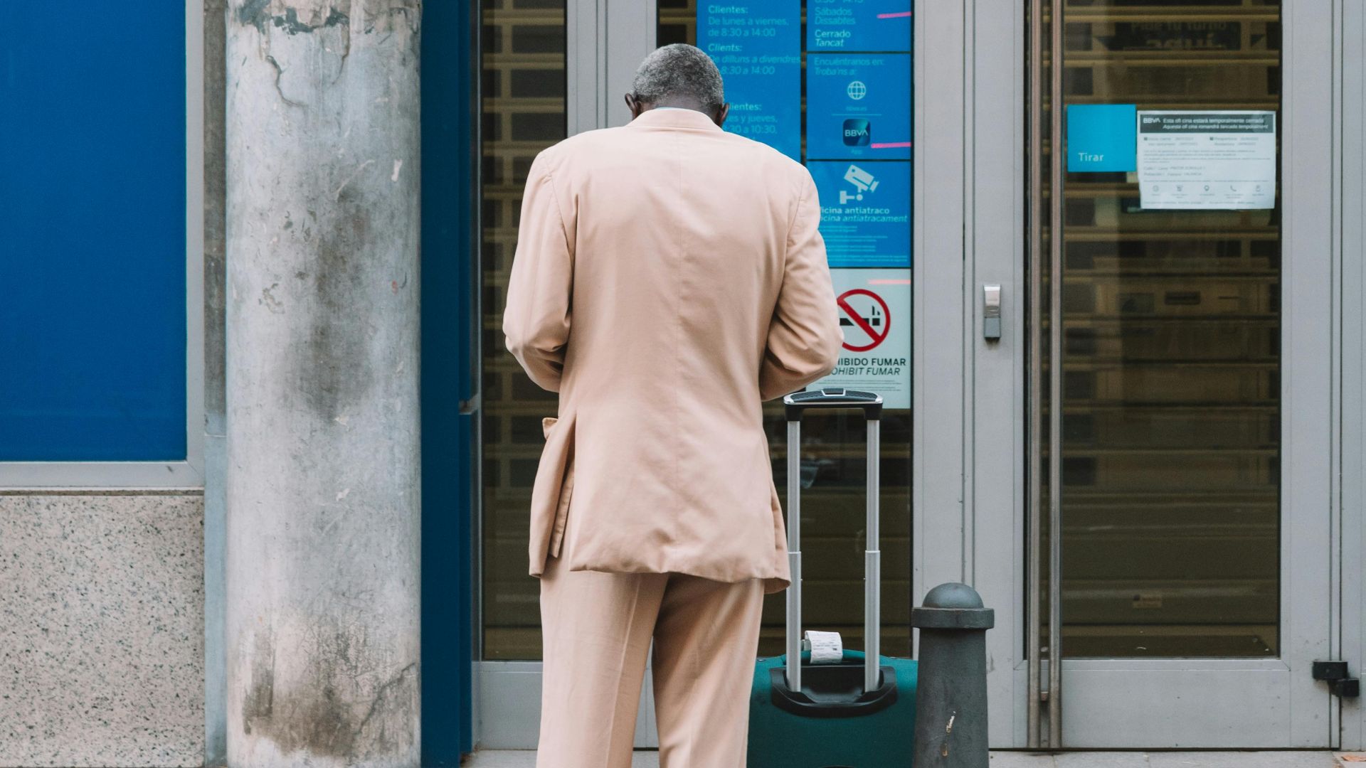 Man in a suit with luggage standing outside a bank in an urban setting