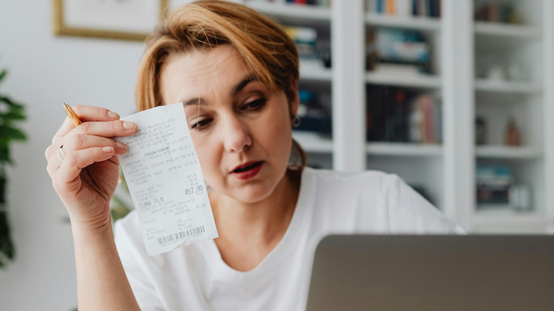Woman using laptop while managing finances with receipts and cash on the table.