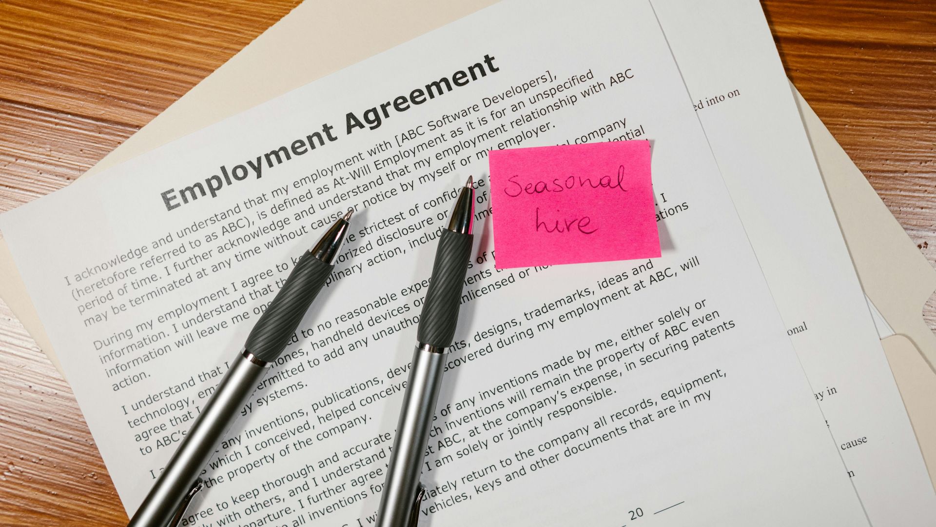 Top view of employment agreement contract with pens and seasonal hire note on wooden desk.