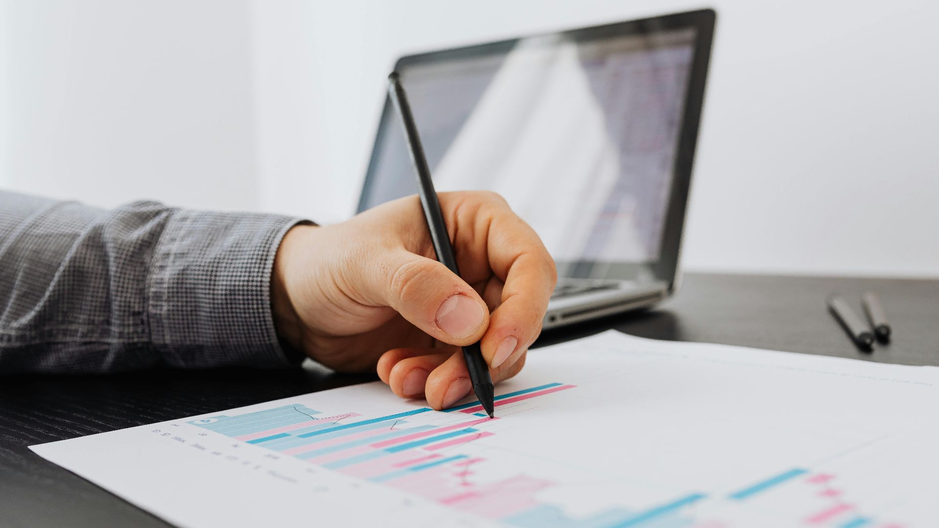 Person taking notes on a business chart with a laptop in the background.