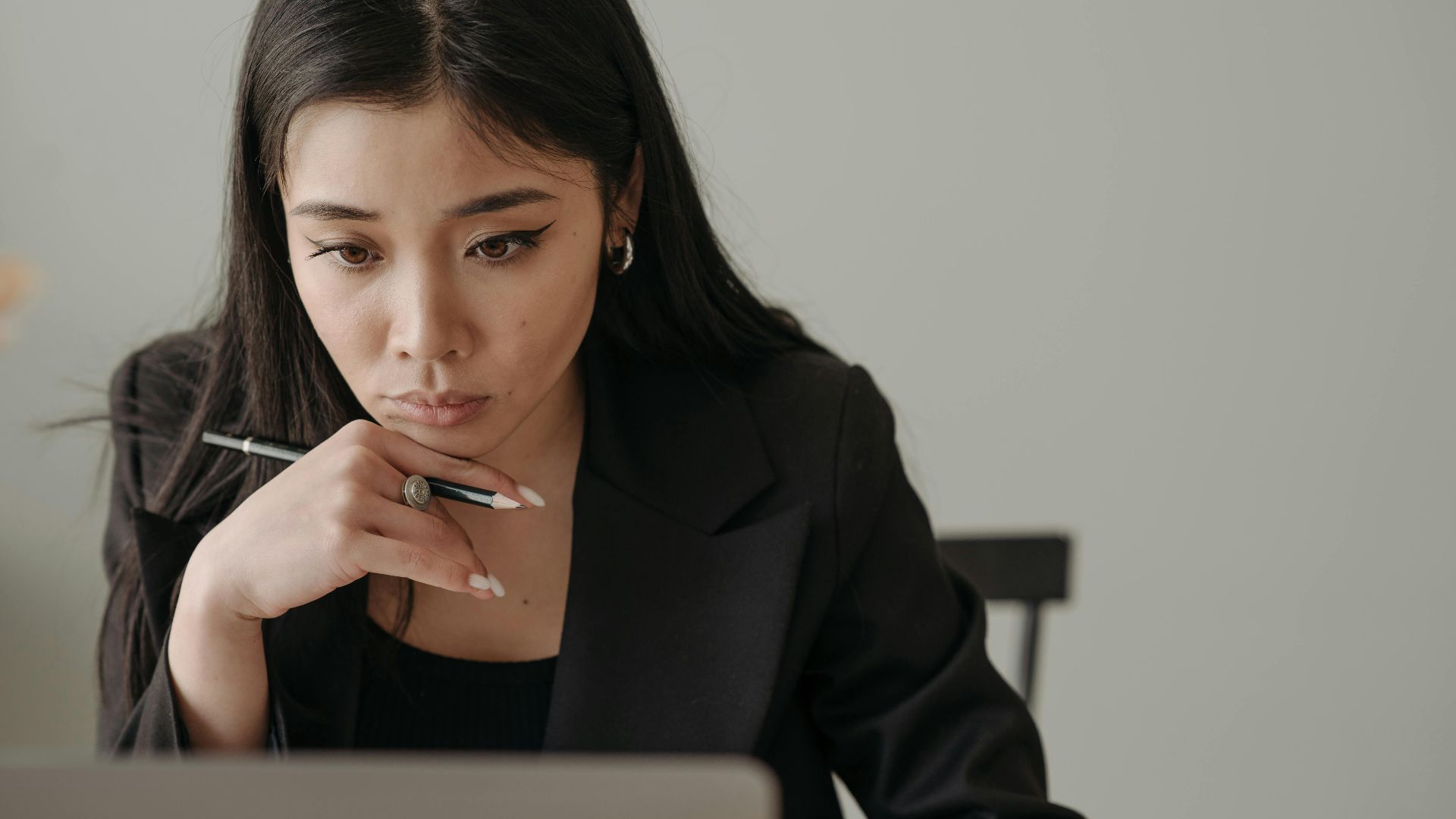 Young woman working remotely, focused on laptop in home office, holding a pencil.
