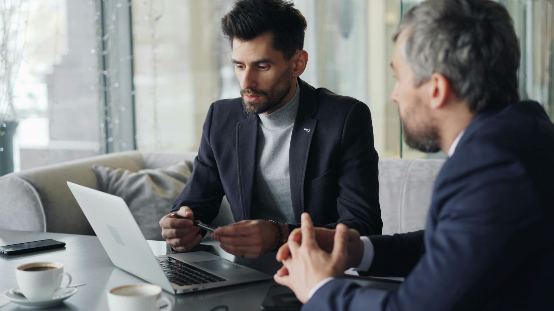 Two businessmen engaged in a meeting in a cozy café, discussing on a laptop.