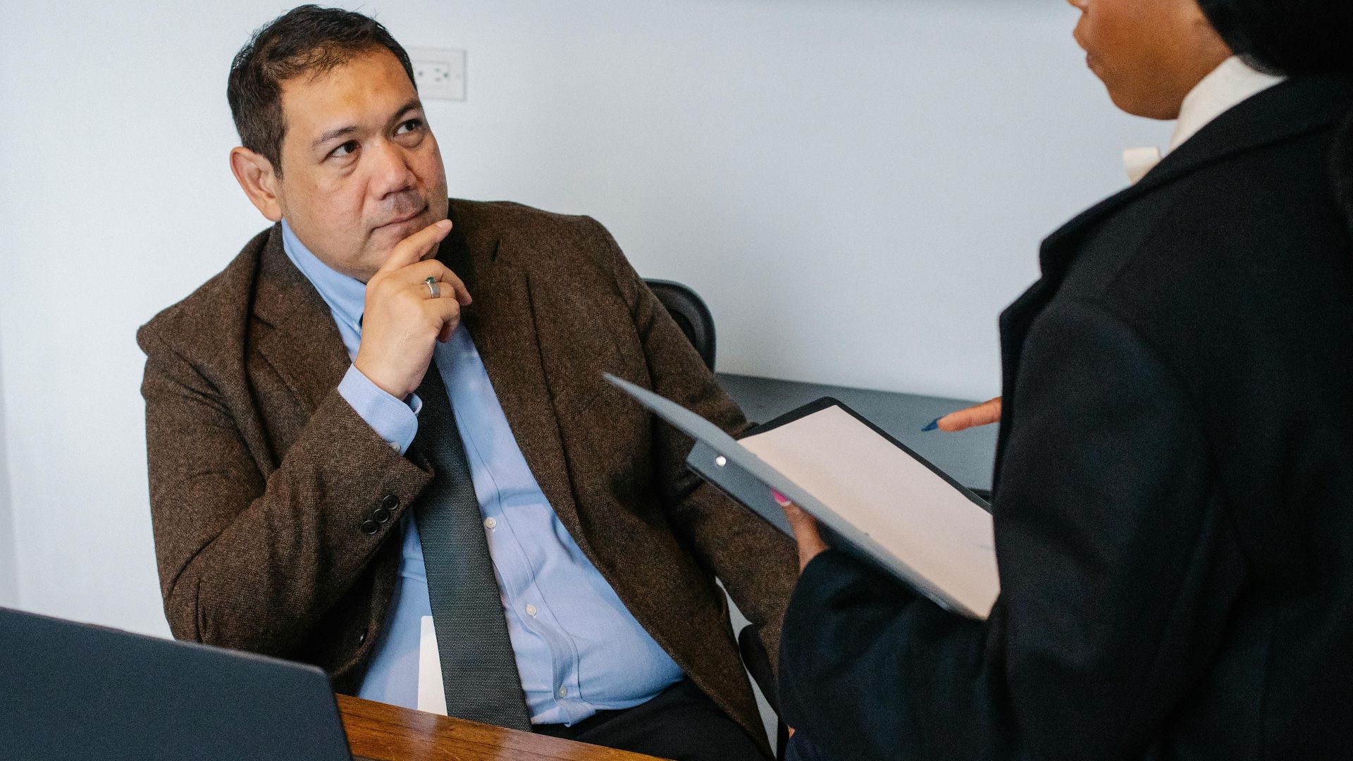 African American female office worker reading report for Asian male manager while working together in contemporary workspace