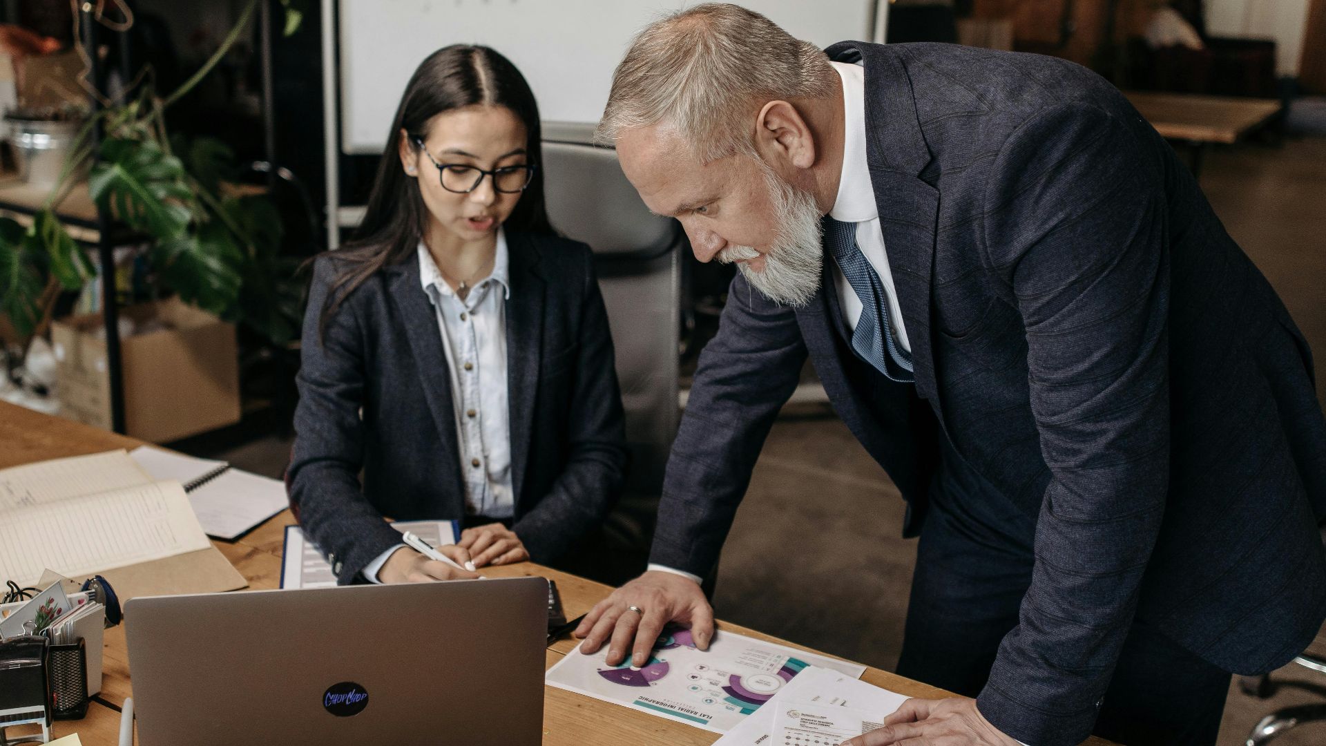 Business meeting with two professionals discussing charts and data at a desk.