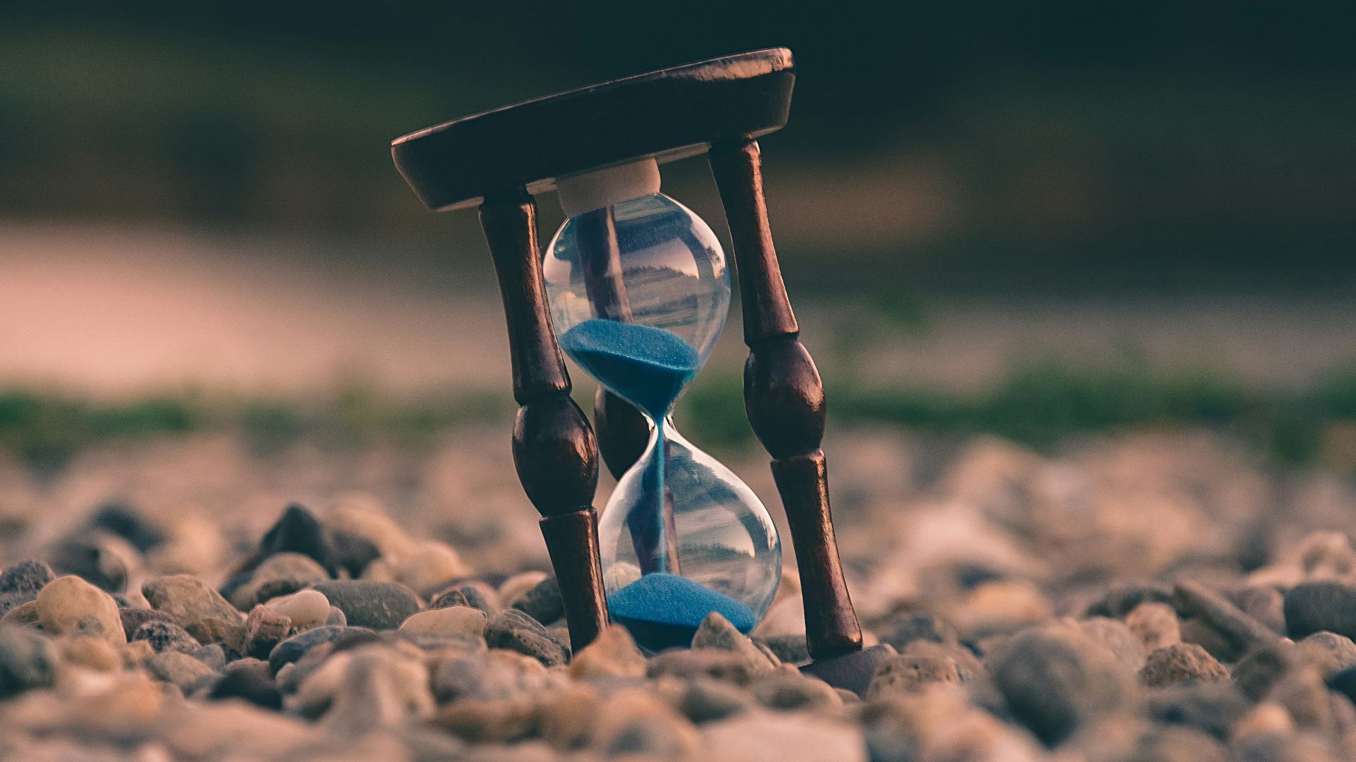 selective focus photo of brown and blue hourglass on stones
