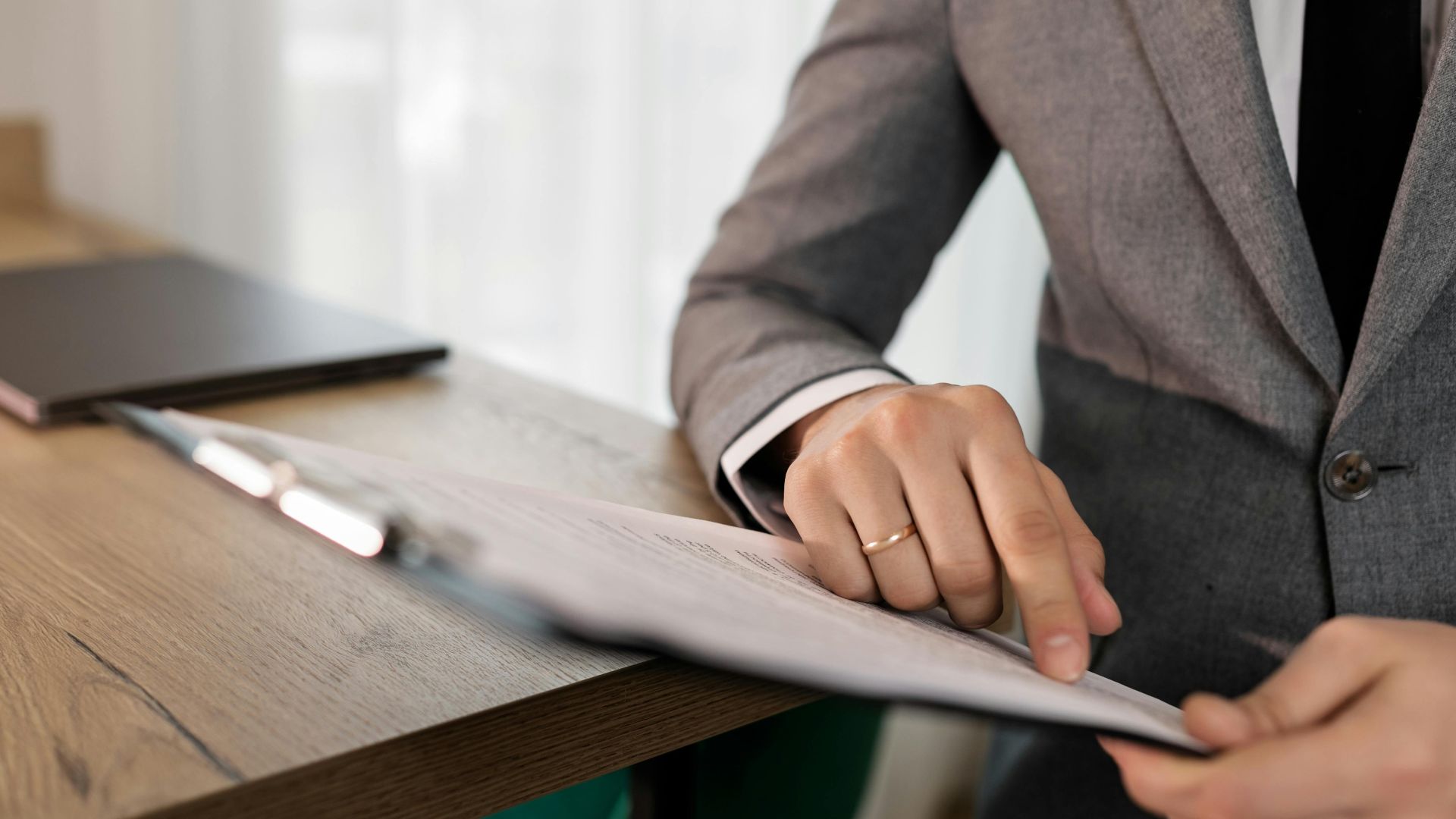 Professional businessman in suit reviewing documents on clipboard at office desk.