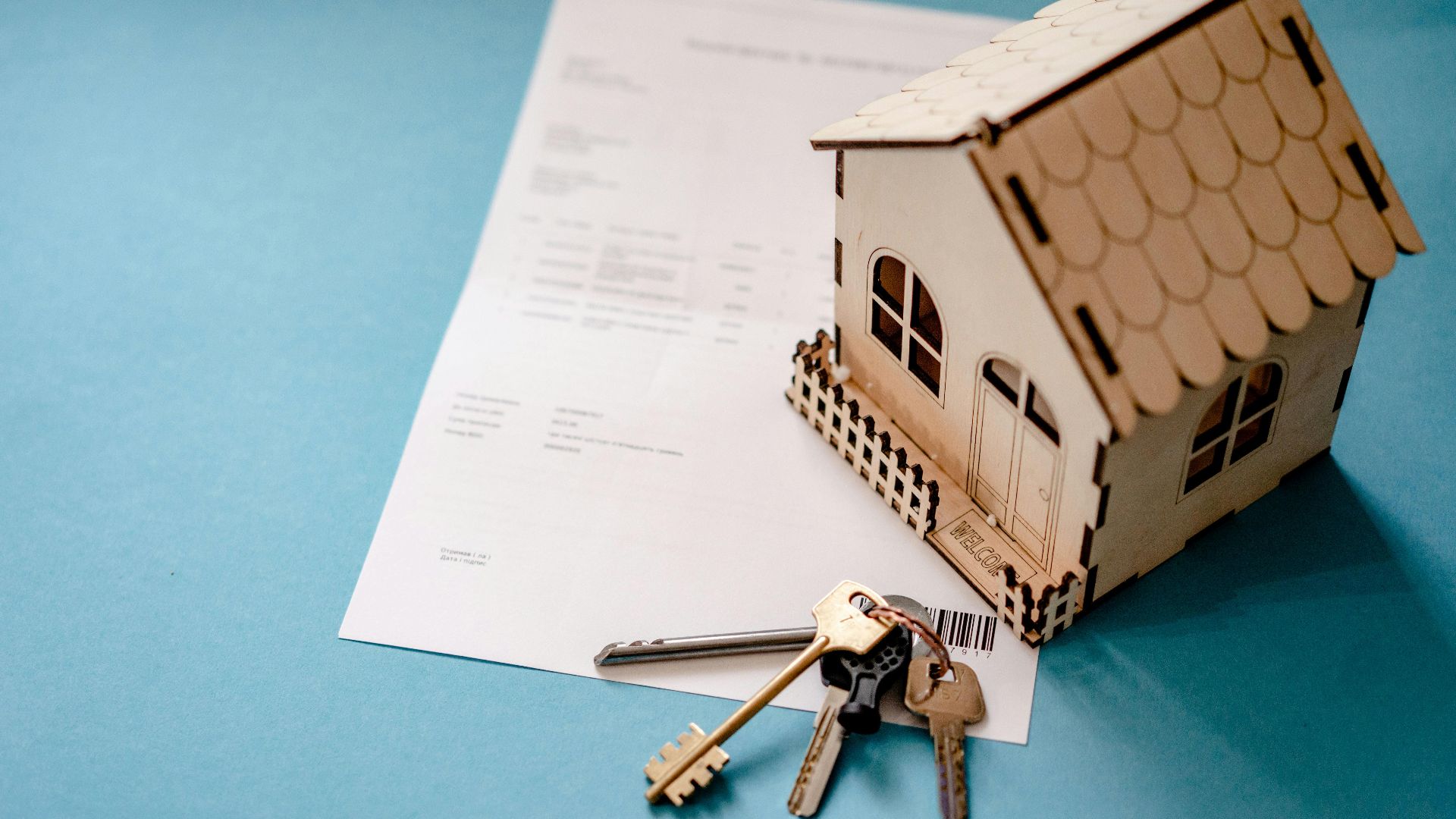 Miniature wooden house with keys and contract symbolizing real estate transactions.