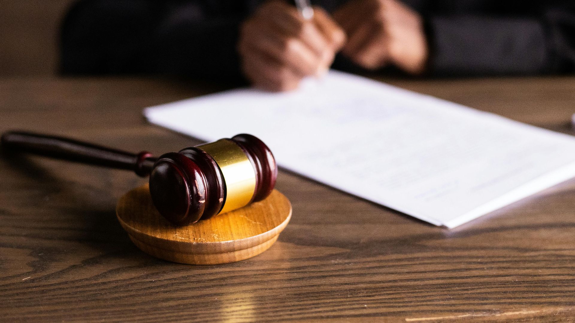 Judge signing documents at desk with focus on gavel, representing law and justice.