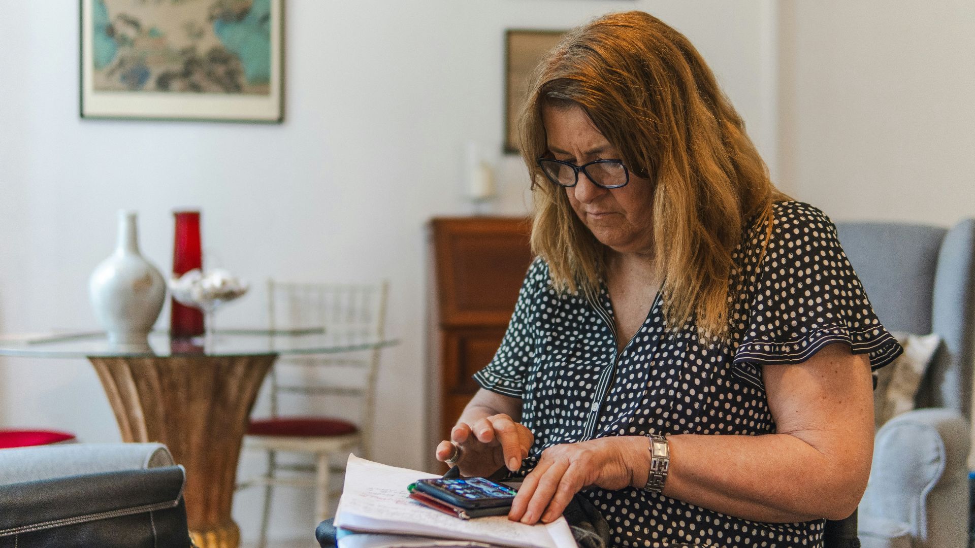 Woman using calculator with papers on table.