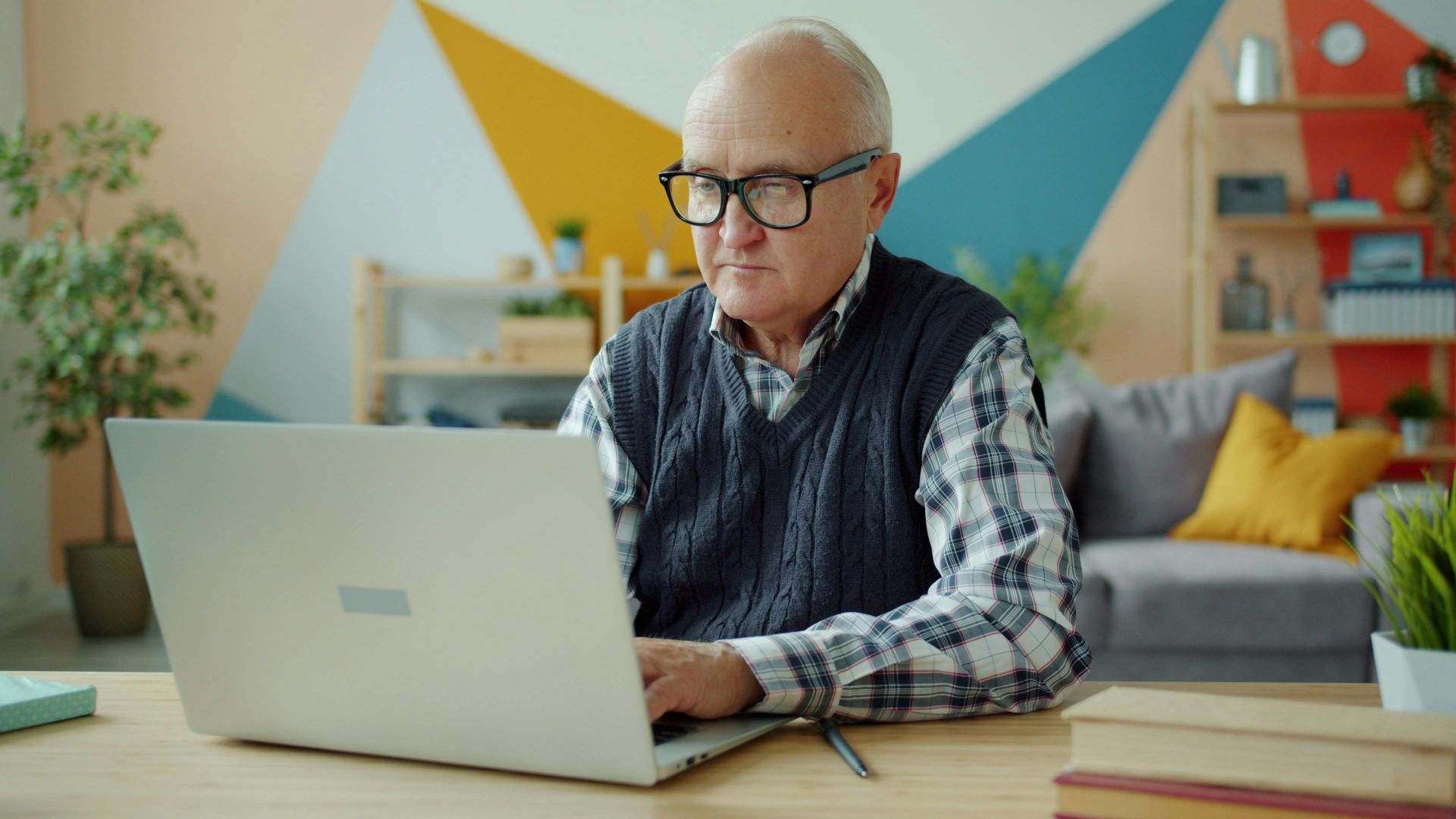Elderly man using laptop in stylish home office, focused and diligent.