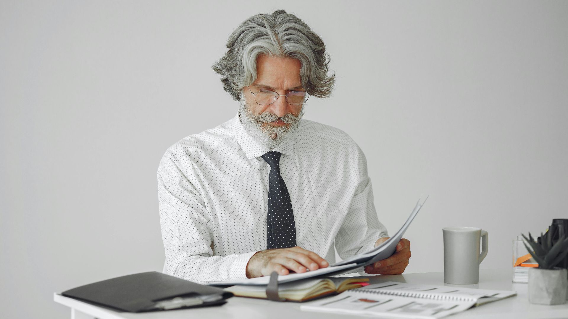 An elderly businessman reviewing documents at his desk in a modern office setting.