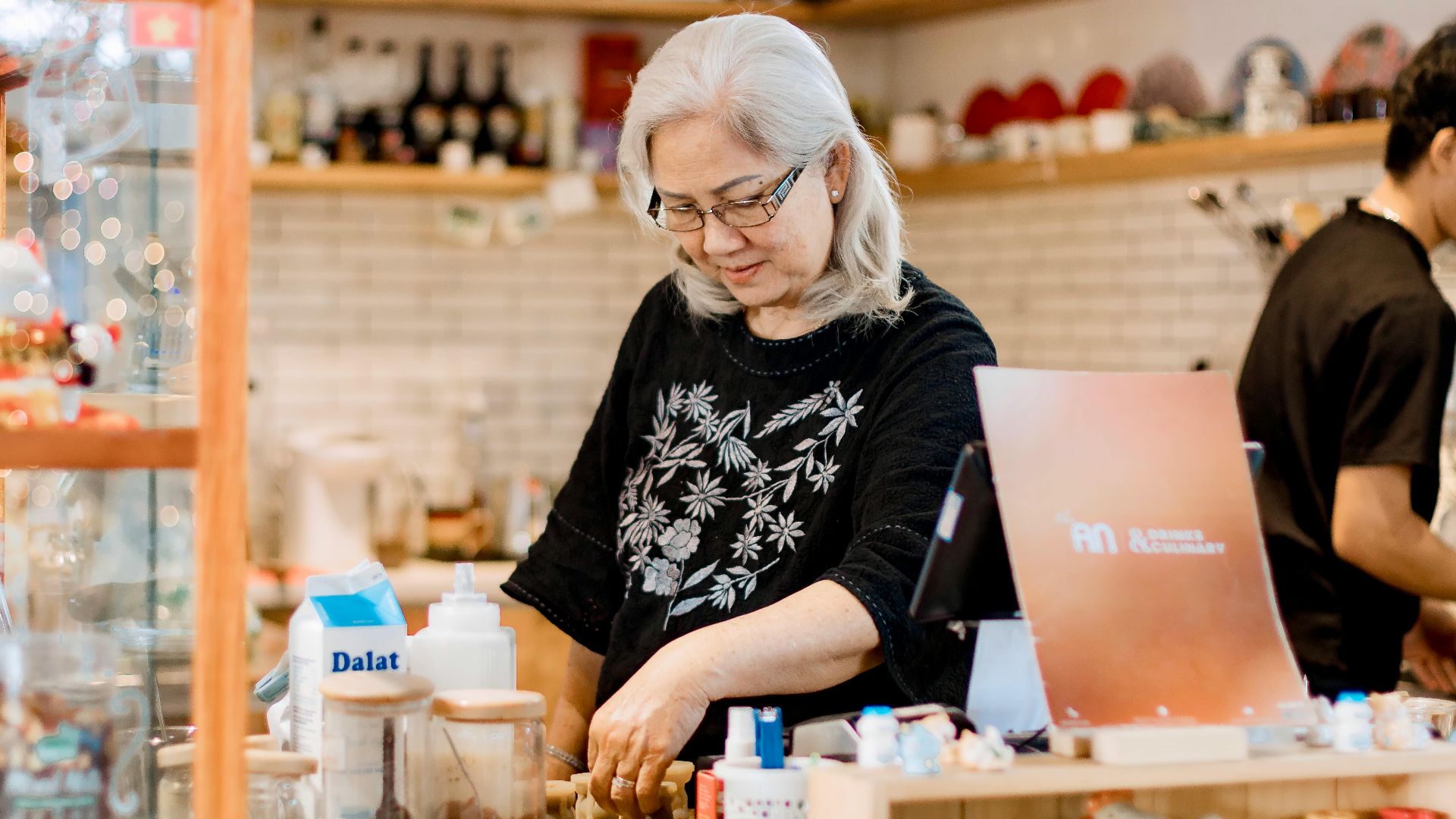 Senior woman working behind the counter in a cozy, warmly lit coffee shop.