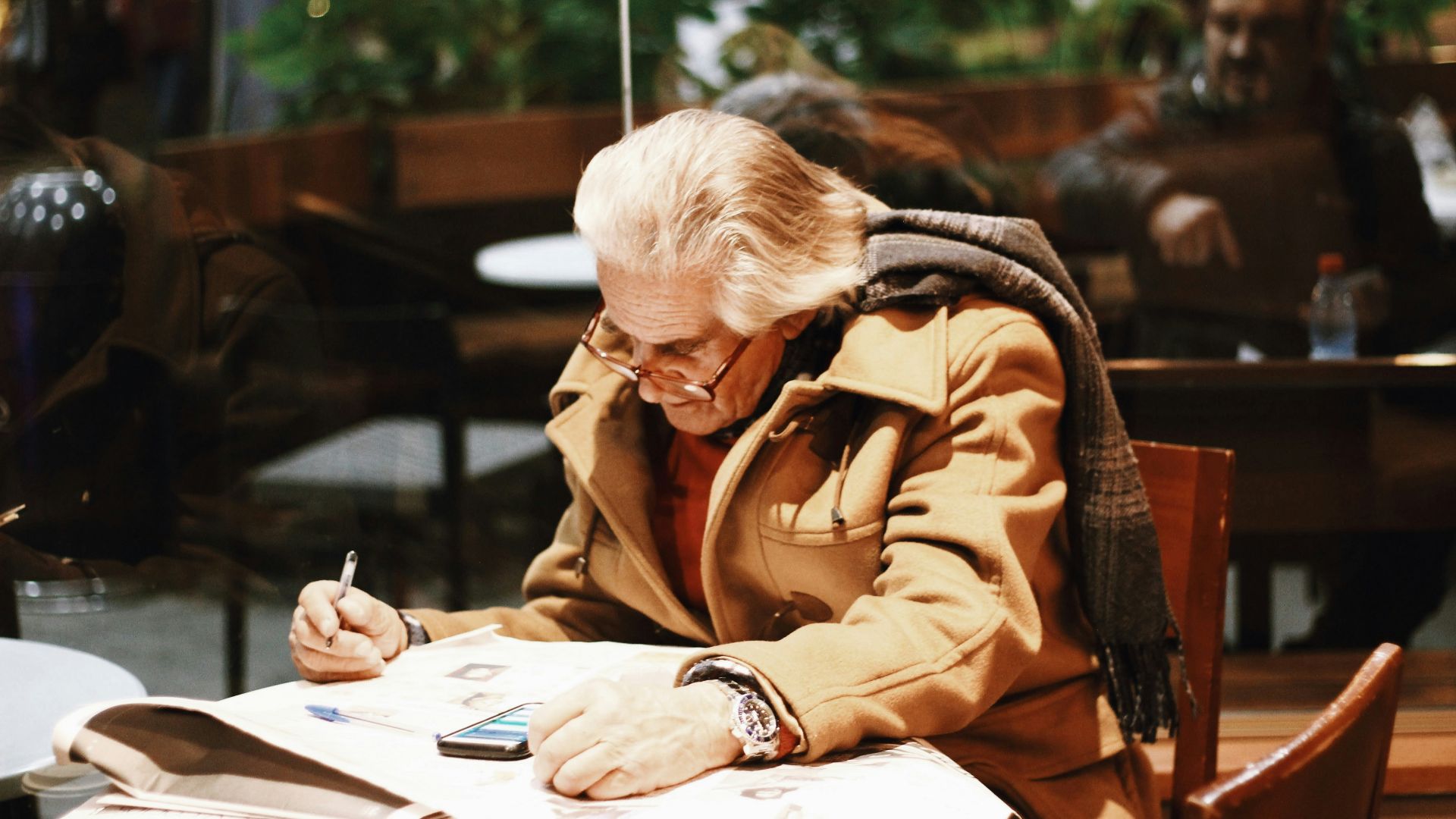 man in brown coat writing on white paper