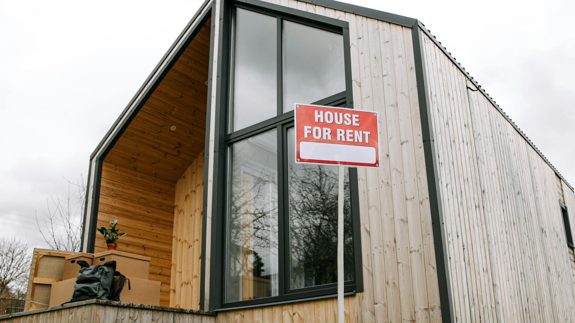 Low-angle view of a modern wooden house with a 'House for Rent' sign, showcasing contemporary architecture.