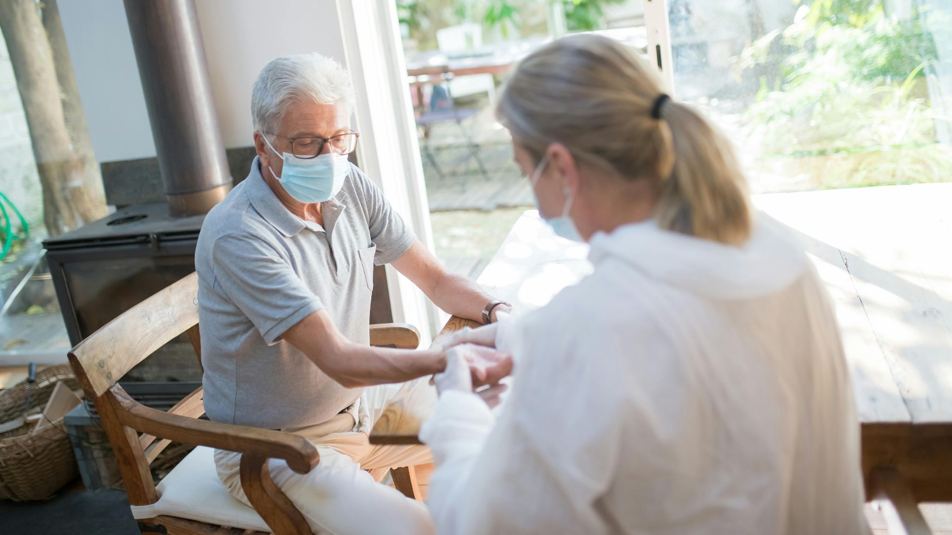 A healthcare worker examining a senior man at home with face masks during the pandemic.