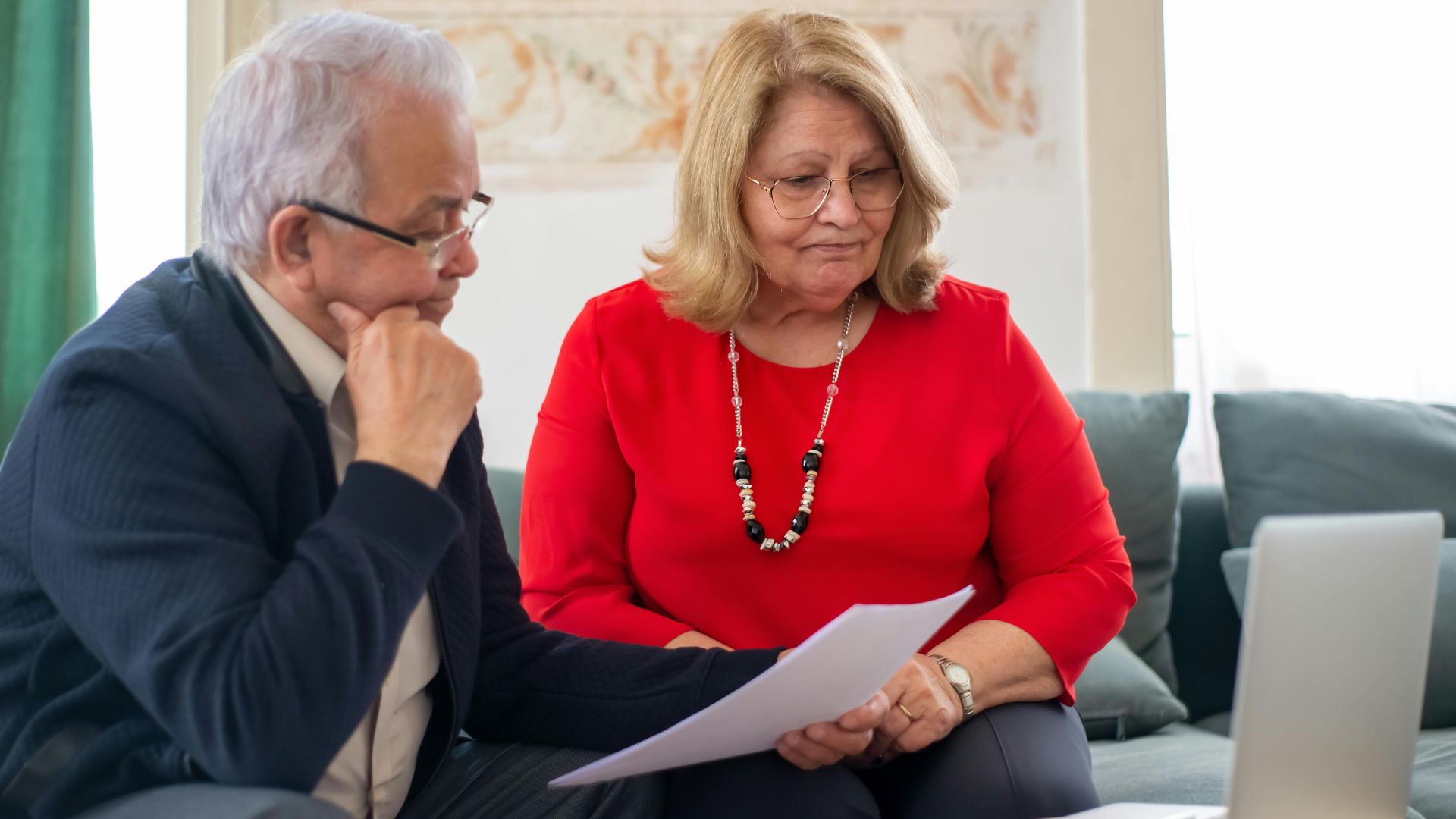 Elderly couple reviewing financial documents together at home in Portugal.