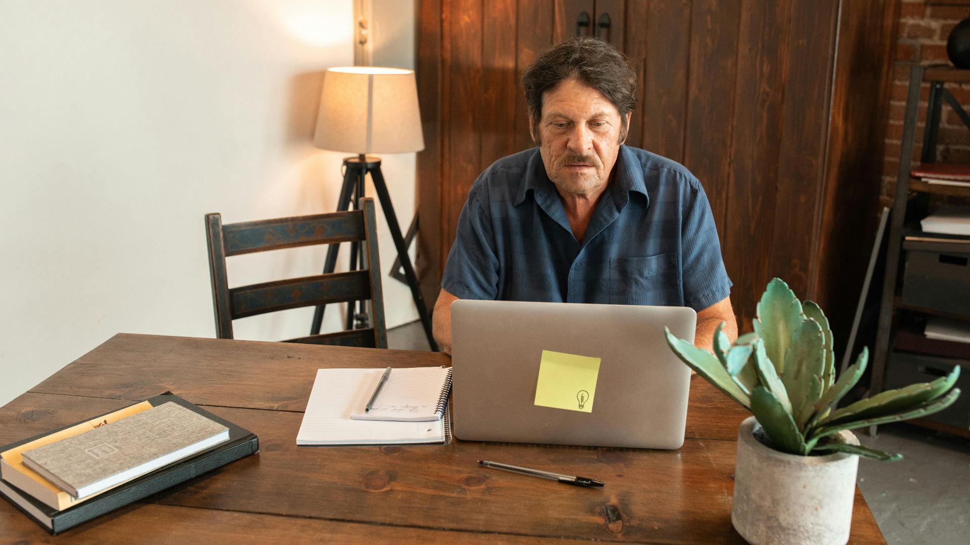 Elderly man focused on a laptop, working from a cozy home office setting.
