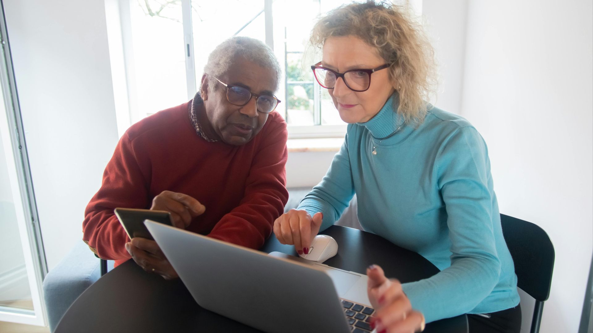 Elderly couple using a laptop in a bright room, focusing on online activities together.